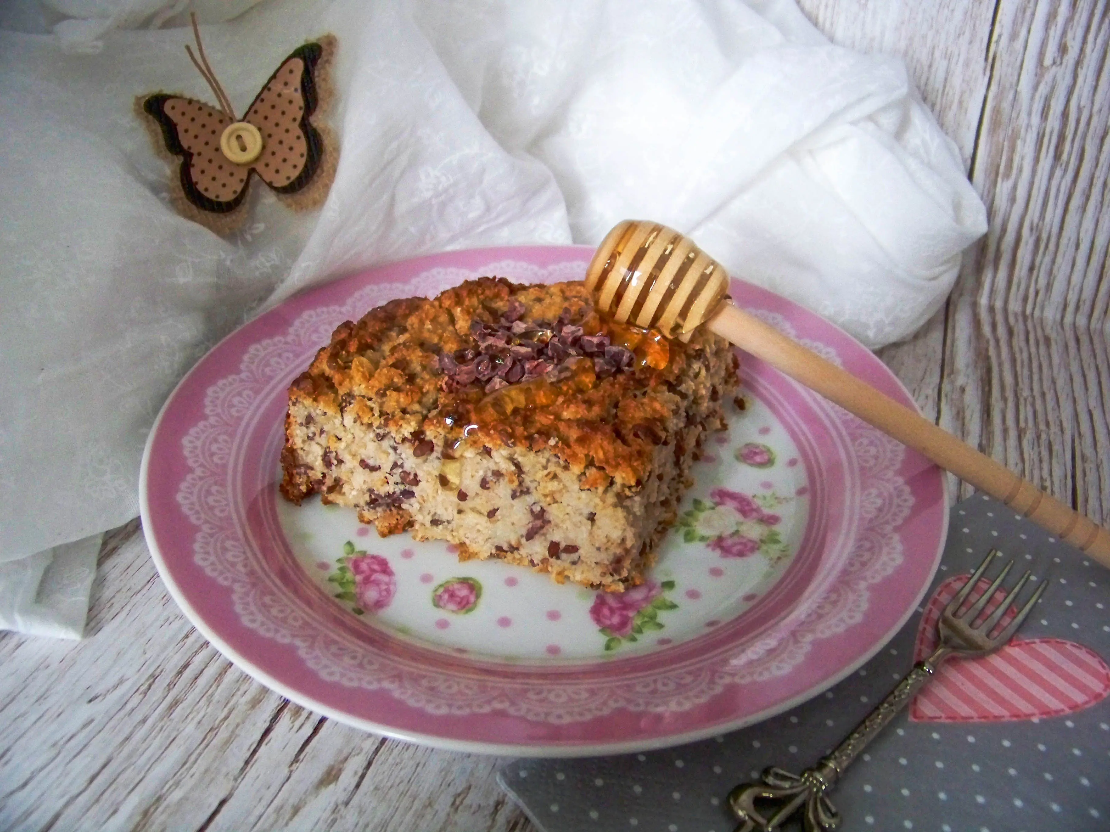 gesunder Frühstückskuchen-mit-rezept-Kakaonibs-Haferflocken-und-Leinsamen - Stück auf einem Teller mit Honiglöffel