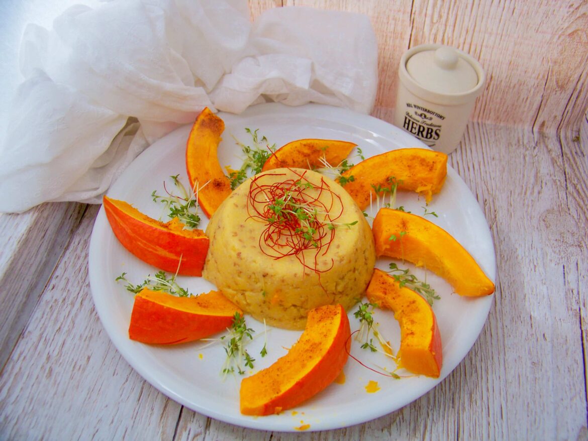 Einfaches Ofenkürbis Rezept mit Sesam-Polenta Ofenkürbis mit Sesampolenta- Kürbisspalten auf einem Teller mit Polentaturm