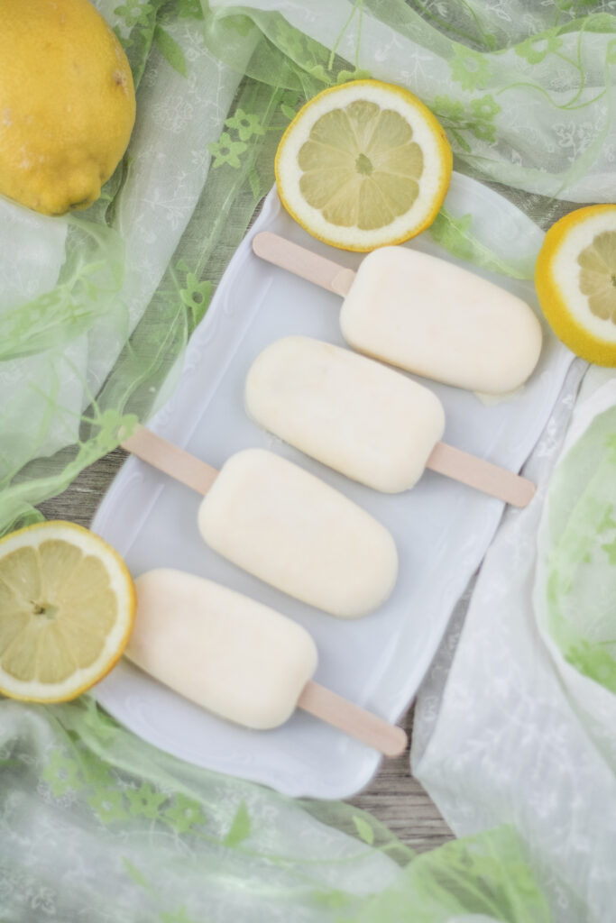 Veganes Zitronen-Mango-Eis am Stil auf einem Teller liegend mit Zitronenscheiben