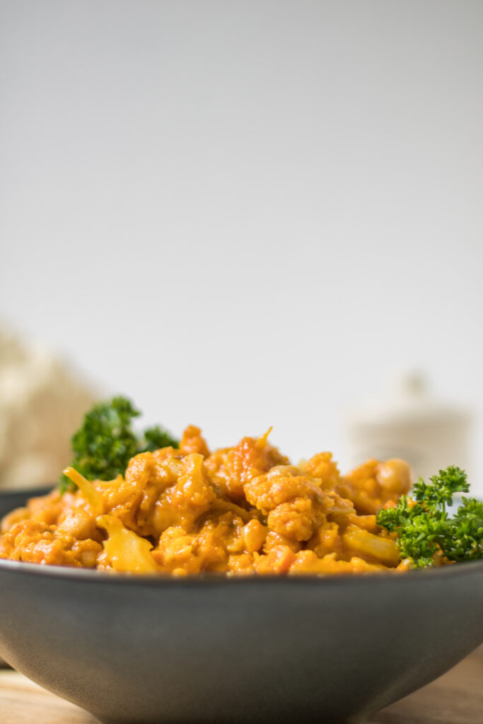 Blumenkohl-Kichererbsen-Curry mit Süßkartoffel in tiefem schwarzem Teller