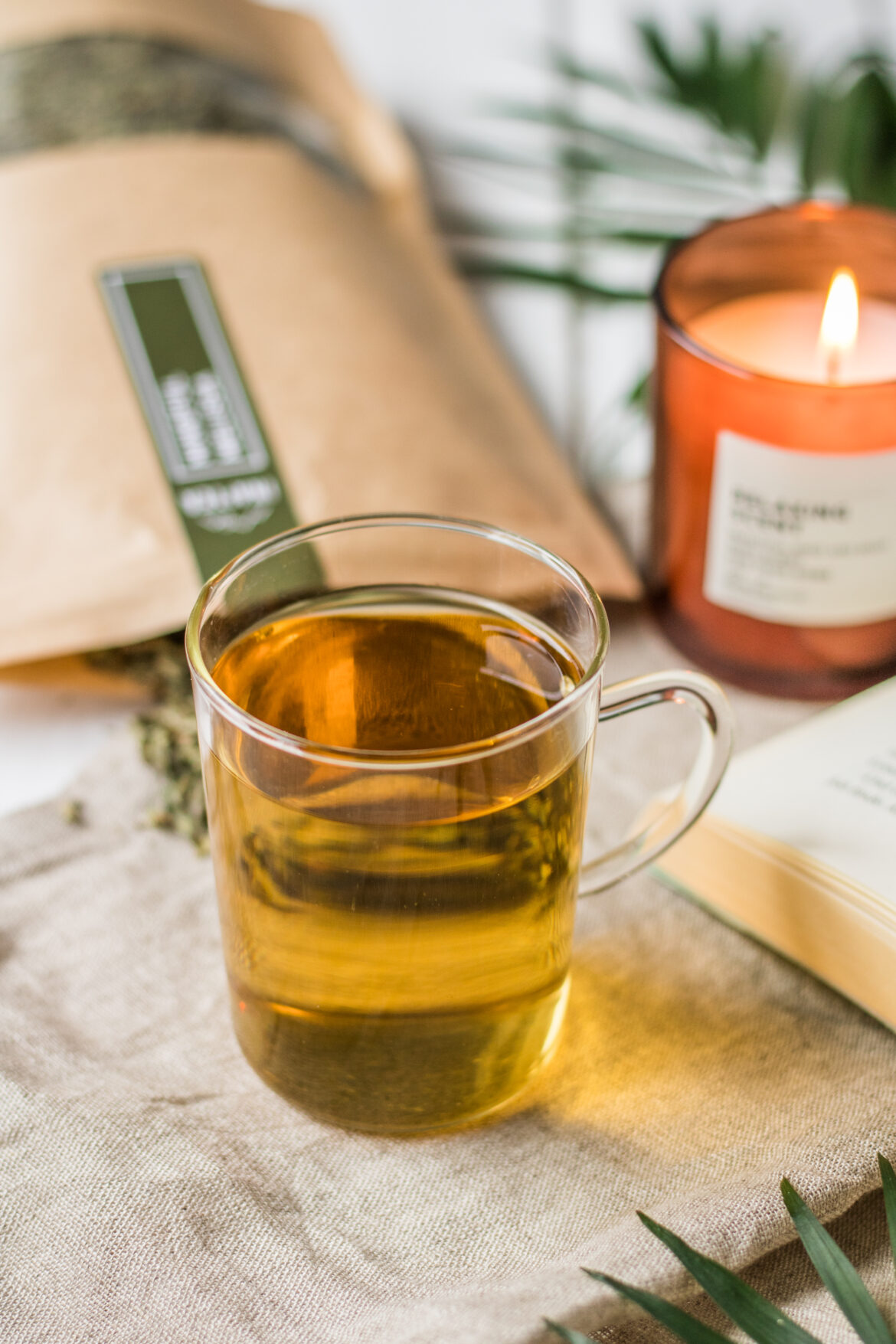 Gesunde Teesorten und ihre Wirkung - Tee im Glas mit Buch und Kerze
